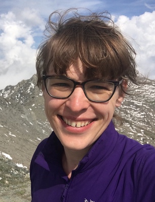 Selfie of a woman wearing a purple hiking jacket in front of a rocky mountain in Queyras region, France